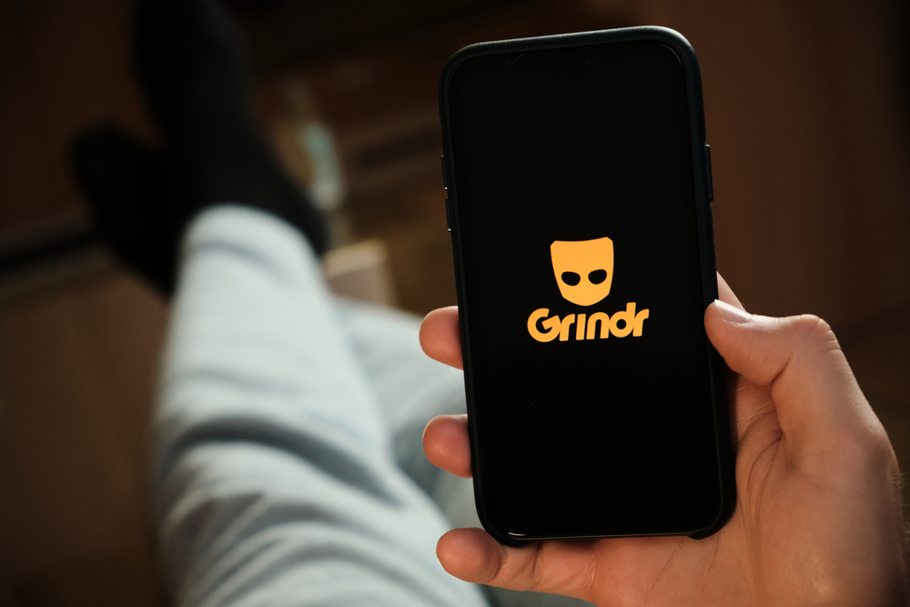 man on phone in bed in the dark lighting up face with grindr dating app
